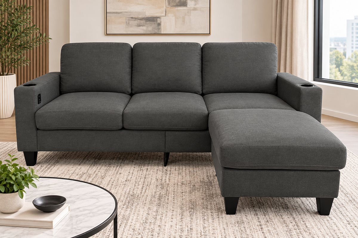 A dark gray fabric sectional sofa with a right-facing chaise lounge, shown in a modern living room setting with a round coffee table, potted plant, and window view.